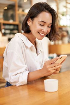 Portrait of young brunette woman, sitting with coffee and using smartphone in a cafe, chatting on mobile phone.