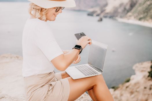 Digital nomad, Business woman working on laptop by the sea. Pretty lady typing on computer by the sea at sunset, makes a business transaction online from a distance. Freelance remote work on vacation