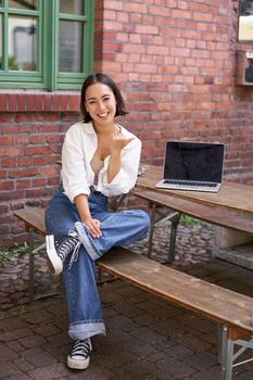 Beautiful asian woman with laptop, sitting and working in cafe, laughing and smiling, drinking coffee. Urban lifestyle and people concept