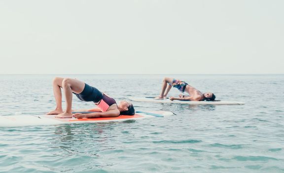 Woman sup yoga. Happy young sporty woman practising yoga pilates on paddle sup surfboard. Female stretching doing workout on sea water. Modern individual female outdoor summer sport activity