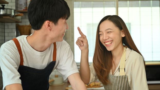 Cheerful young husband and wife have fun together in kitchen, enjoying spending free weekend time together at home.