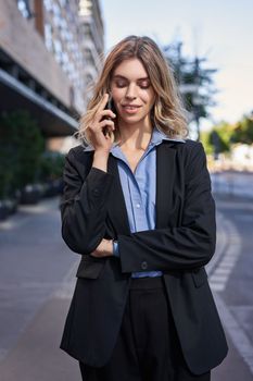 Vertical shot of confident young businesswoman making phone call, standing on street and talking on telephone.