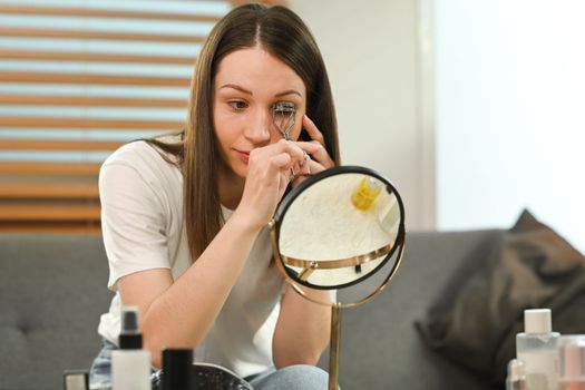 Charming caucasian woman in casual clothes using eyelash curler curling eyelashes. Beauty care and Cosmetics concept.