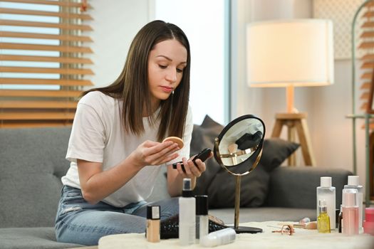 Pretty caucasian woman in casual clothes applying powder puff and looking mirror. Beauty, cosmetology and skincare concept. 