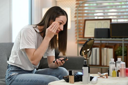 Pretty caucasian woman applying face powder with puff while looking in mirror. Beauty care and Cosmetics concept.