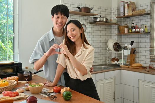 Happy loving couple making heart shape with their hands and smiling to camera, enjoying leisure time at home. 