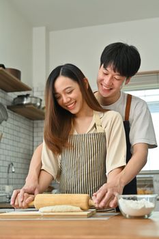 Loving asian husband and wife have fun making bread in modern kitchen, enjoying spending free weekend time together.