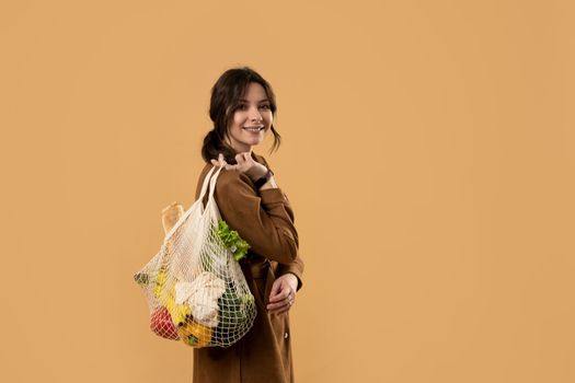 Young brunette woman holding reusable cotton shopping mesh bag with organic groceries from a market. Concept of no plastic. Zero waste, plastic free. Sustainable lifestyle