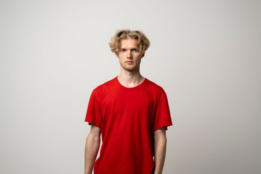 Handsome young man in blank red shirt against white wall. Clothing design concept