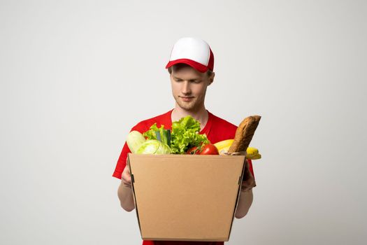 Handsome young delivery man carrying package box of grocery food, fruits, bread and drink from store. Delivery concept