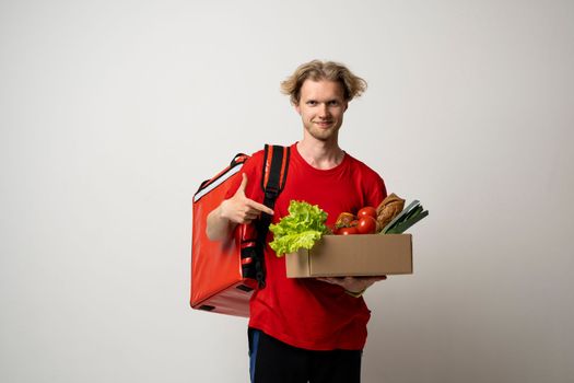 Delivery concept. Handsome young delivery man with a thermal bag carrying package box of grocery food and drink from store