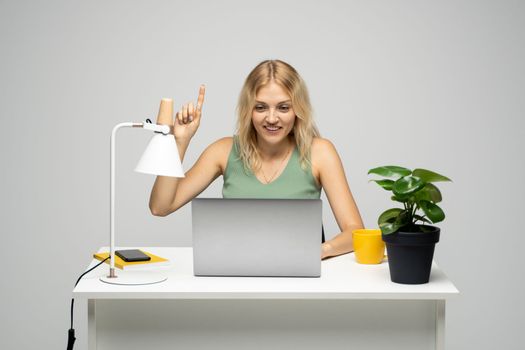 Woman pointing finger up and smiling toothy while sitting at a table with a laptop. Having idea, business plan, startup concept