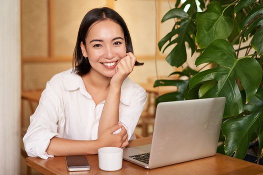 Smiling female manager, freelancer or student sitting with laptop in cafe and working, typing on computer.