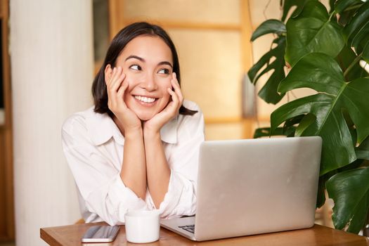 Confident young stylish woman with laptop, sitting in cafe and working, freelancer in co-working space with cup of coffee.