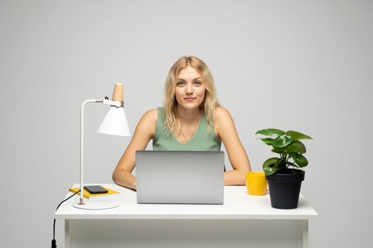 Portrait of attractive blonde woman business woman, entrepreneur, freelancer sitting at a table with a laptop computer