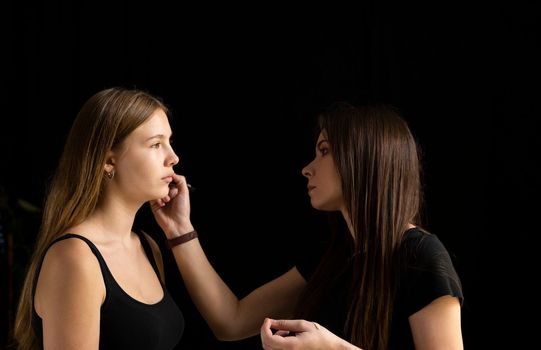 Makeup artist applies a make up on a model face. Beautiful woman with make-up face. Hand of visagiste, painting cosmetics of young beauty model girl. Make up in process