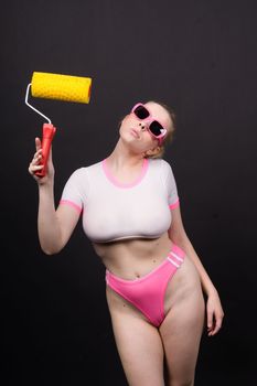 Beautiful blonde model wearing short dress bodysuit is holding a roller brush.