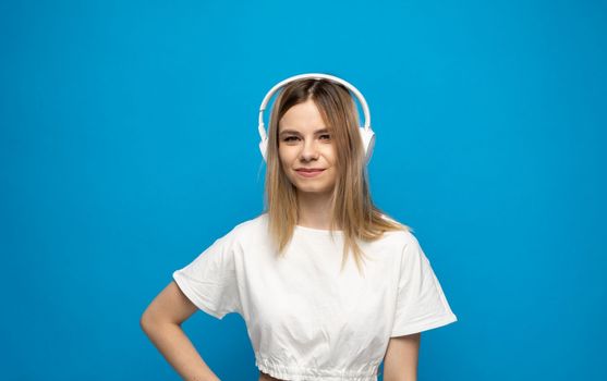 Beautiful bonde young woman in white headphones listening to music on blue background
