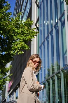 Portrait of confident saleswoman going to work, wearing sunglasses and suit. Businesswoman on her way to office, posing outdoors.