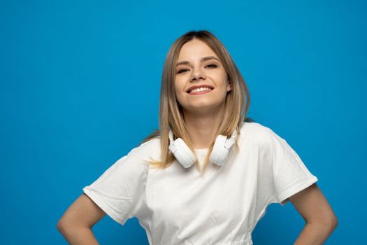 Beautiful blonde young woman with a white headphones on a shoulder on blue background