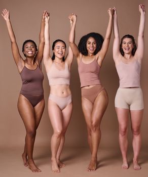 Diversity, women and natural beauty friends in studio in brown background with hands raised in celebration and support together. Diverse woman, underwear and celebrate body care or healthy lifestyle.