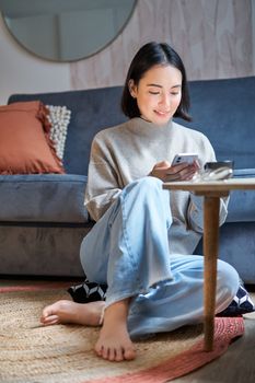 Technology and people. Young stylish asian woman sits at home with her smartphone, texting message, using application on mobile phone.