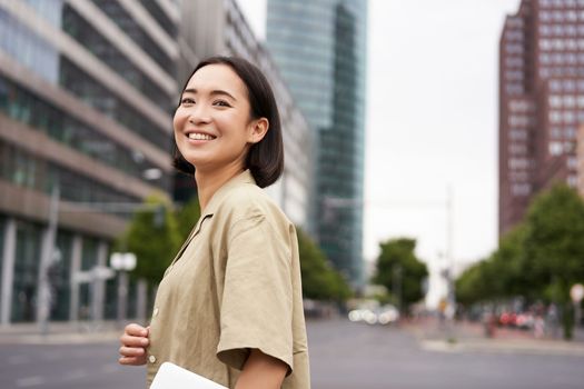 Outdoor shot of asian girl with laptop, going somewhere in city centre, walking on street, going to work.