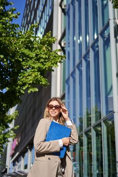 Portrait of confident saleswoman going to work, wearing sunglasses and suit. Businesswoman on her way to office, posing outdoors.