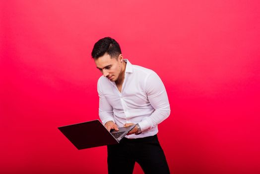 Image of young cheerful businessman holding and using laptop isolated over red background