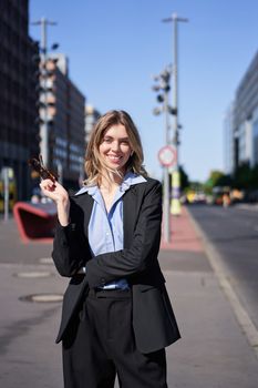 Portrait of successful young company ceo, businesswoman in black suit, standing on sunny street and smiling. Corporate people