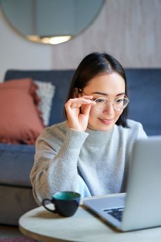 Young asian girl, freelancer professional sitting in living room and working with computer, studying at home using computer.