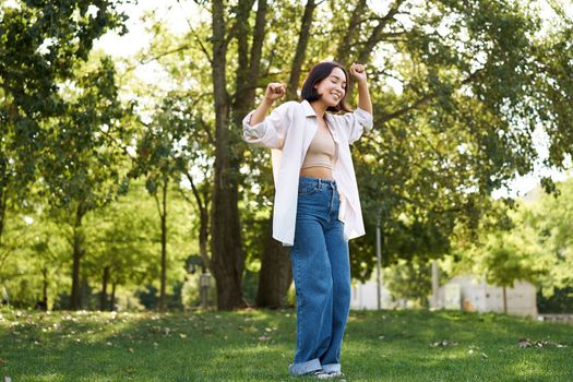 Happy people. Carefree asian girl dancing and enjoying the walk in park, feeling happiness and joy, triumphing.