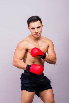 Muscular model sports young man in a boxing gloves on grey background. Male flexing his muscles.