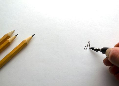 A woman writes with black ink on paper. The hand draws with black ink on white paper, pencils lie on the left.