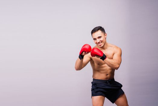 Muscular model sports young man in a boxing gloves on grey background. Male flexing his muscles.