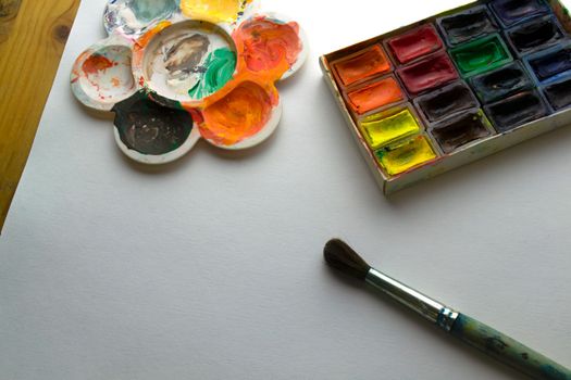 Paints, brush, palette and paper on the table. Watercolor paints, brush, palette and paper on the table.