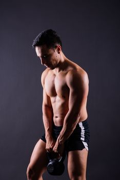 Sporty man working out with kettlebell. Photo of man on dark background. Strength and motivation