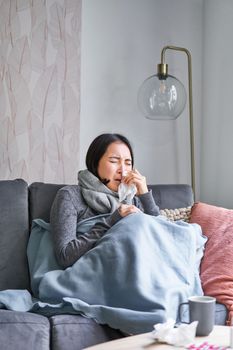 Korean woman feels unwell, sneezing and coughing, catching cold, staying at home with fever and temperature, taking medication.