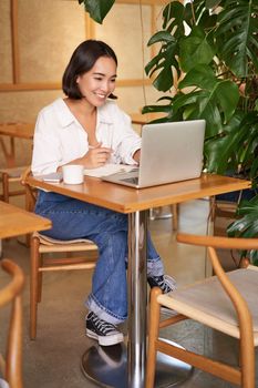 Stylish businesswoman with laptop, sitting in cafe and working on computer, managing business and drinking coffee.