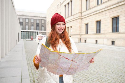 Redhead girl, tourist explores city, looks at paper map to find way for historical landmarks, woman on her trip around euope searches for sightseeing.