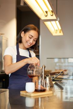 Cute korean barista girl, pouring coffee, prepare filter batch brew pour over, working in cafe. Workplace and people concept