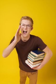 College Education Concept. Student Invites Applicants to Study. A Young Man with Books on a Yellow Background. High quality photo