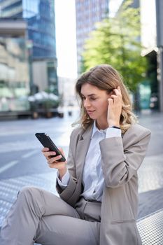 Vertical portrait of woman in suit using mobile phone, reading message or checking app, posing outdoors.