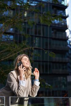 Vertical shot of businesswoman on a call, standing outside business center, talking on mobile phone.