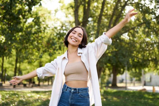 Carefree woman dancing and walking in park with hands lifted up high, smiling happily. Lifestyle concept.