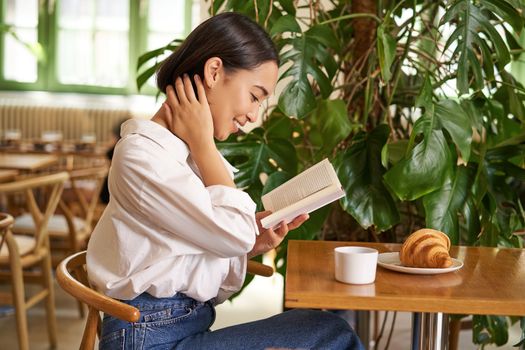 Tender, beautiful asian girl sitting with a book in cafe, reading and drinking coffee. People and lifestyle concept.