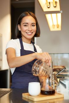 Vertical shot of smiling korean barista, pouring filter coffee, prepare batch brew for client in cafe, pour over method.