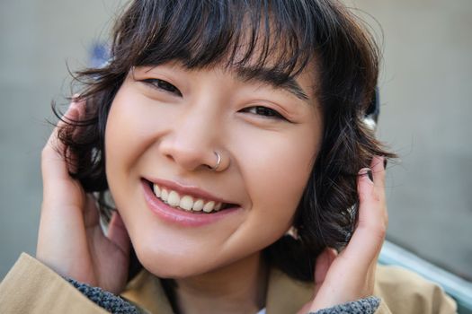 Portrait of happy woman, korean girl in headphones, listening music in headphones, enjoying sound of earphones, laughing and smiling.