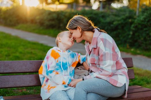 mother and son sit on a park bench in the rays of the setting sun. the concept of a family. Mother's Day. beautiful girl (mother) with a boy (son) in the park in the park are sitting on a bench at sunset.