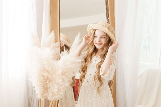 A beautiful teenage girl with long hair measures a straw hat in front of a mirror. Self-admiration of a blonde. selective focus